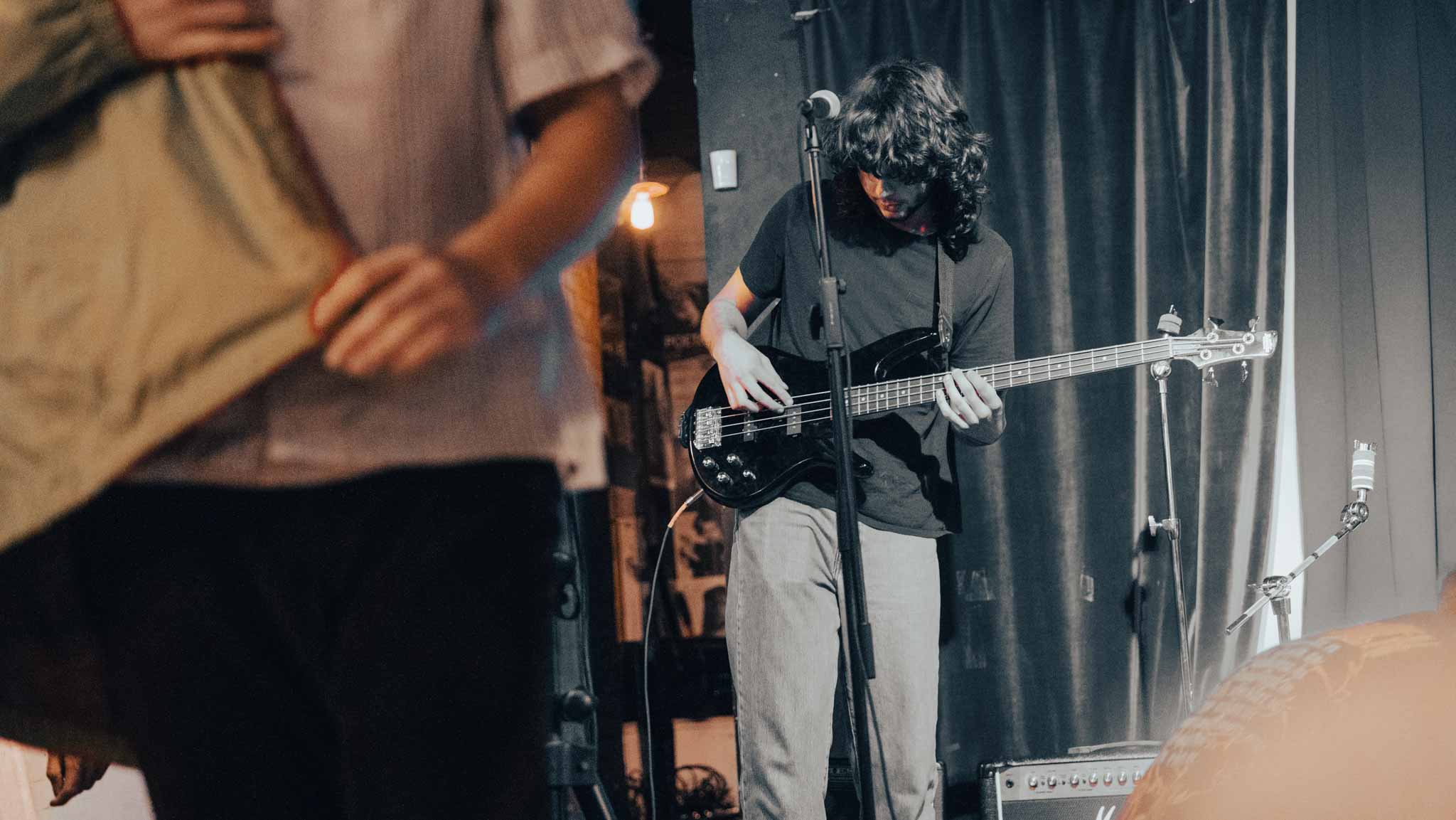 Bassist playing under warm stage light with another performer in the foreground