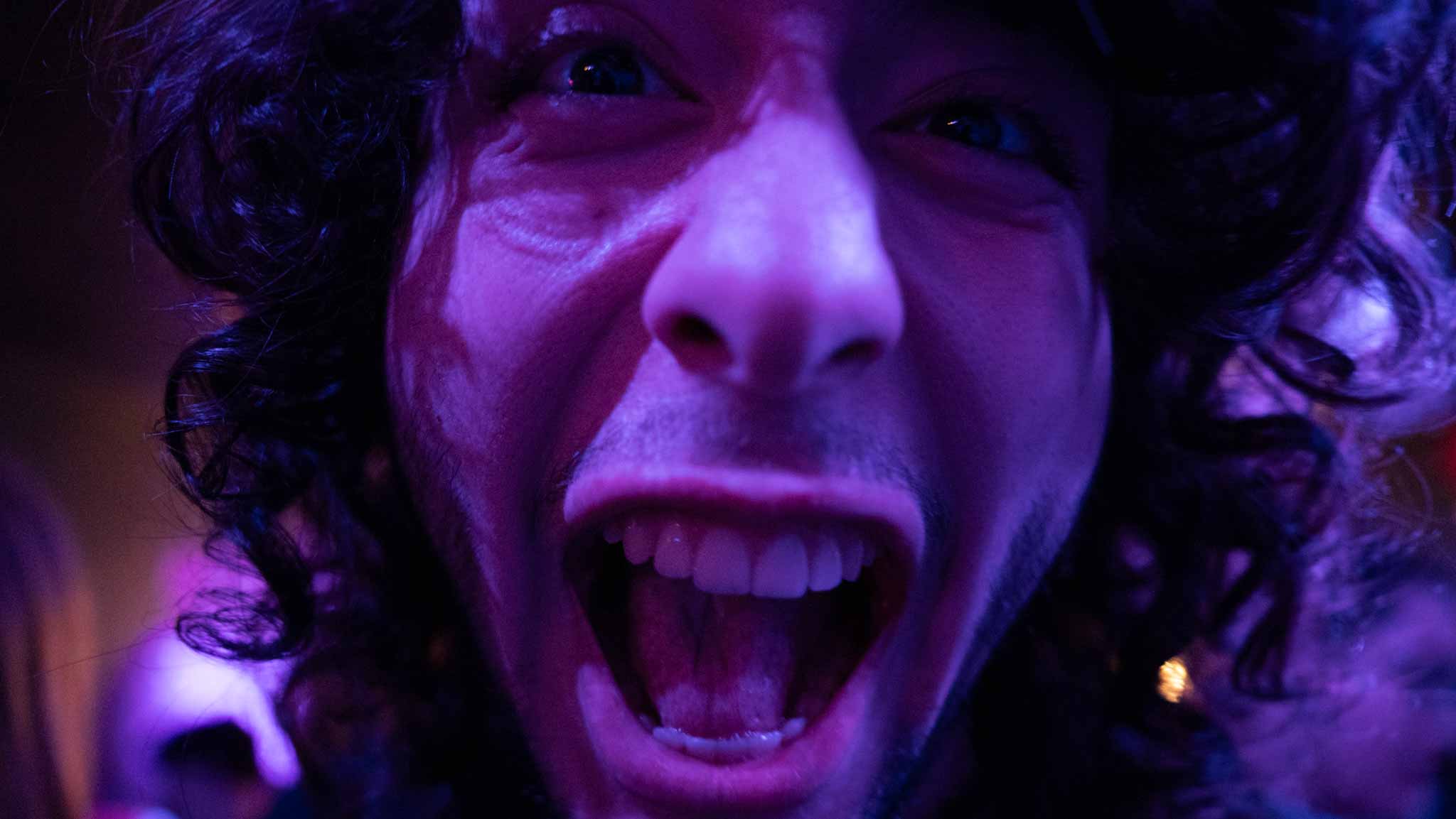 A musician making a playful face close to the camera under violet light