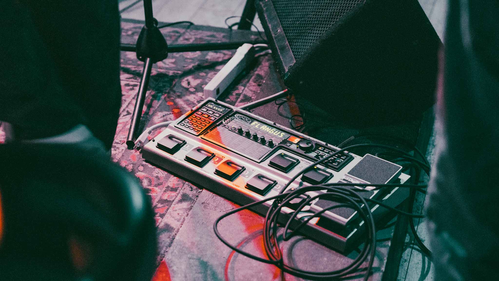 A pedalboard and coiled cables on a patterned stage rug
