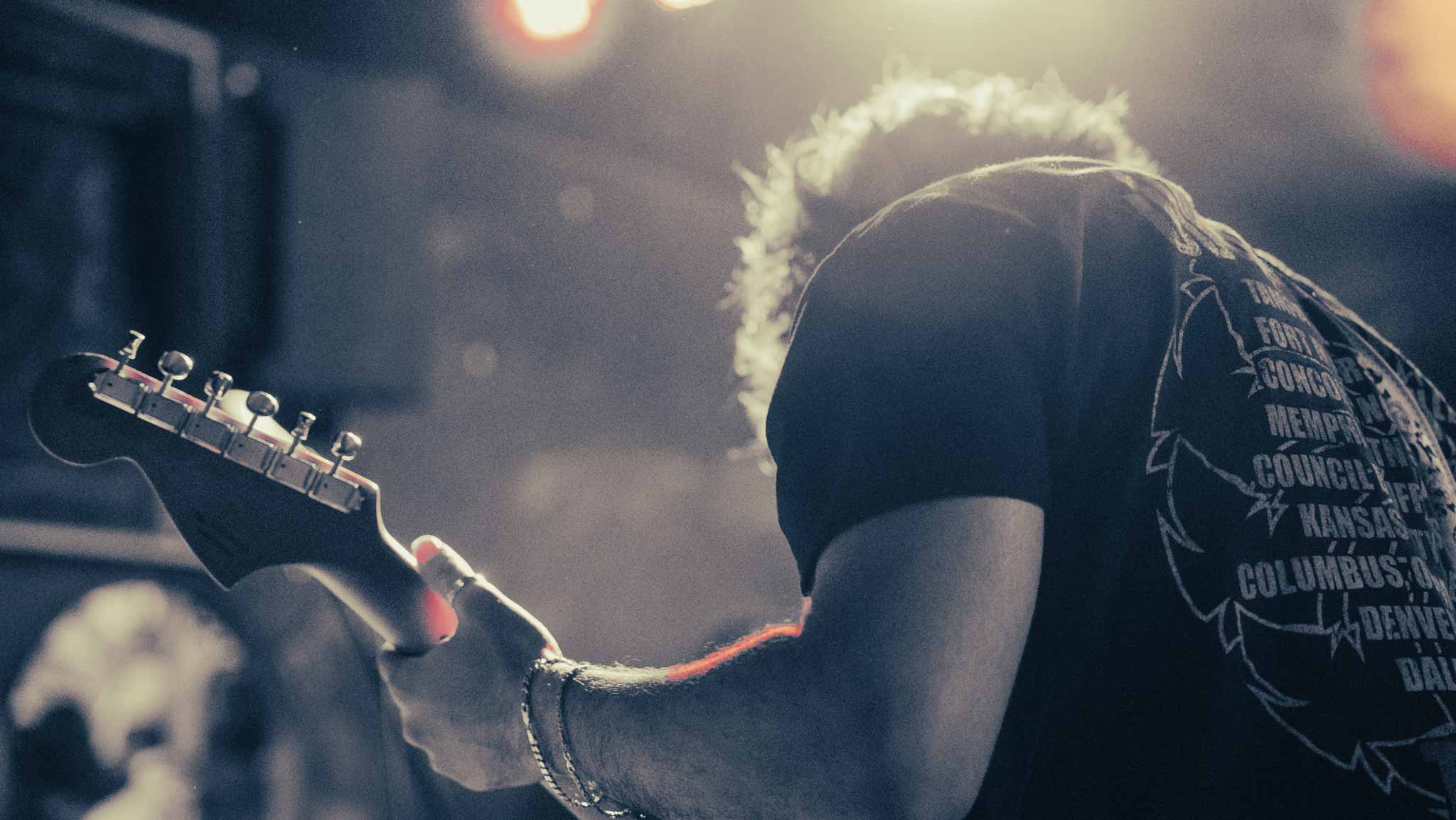 Backlit guitarist bent over the instrument in white stage light