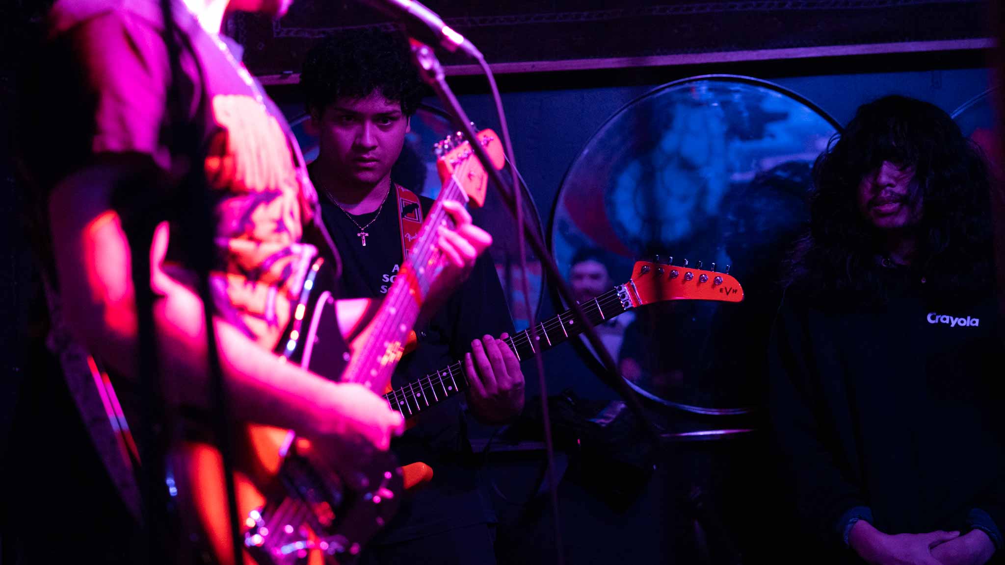 Three band members playing together in magenta and blue light